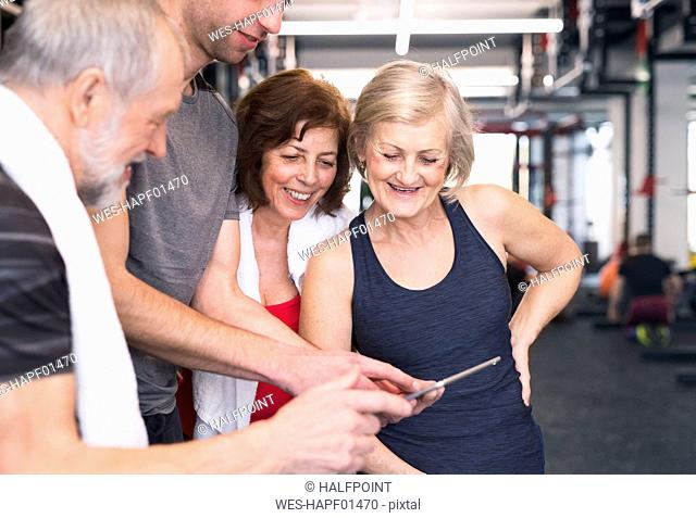 Group of fit seniors and personal trainer in gym looking at tablet