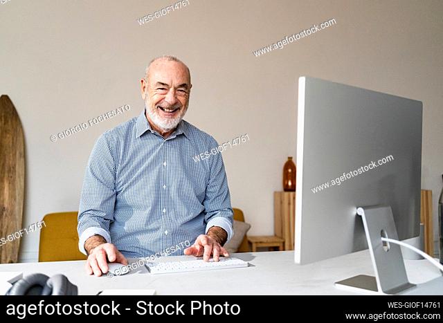 Happy senior freelancer with computer sitting at desk