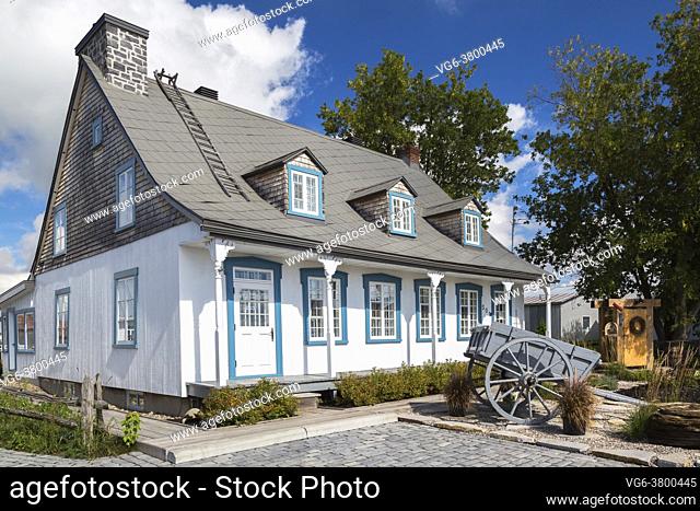 Old circa 1790 white painted vertical pine wood with blue trim Canadiana cottage style home facade with grey sheet metal roof in summer, Quebec, Canada