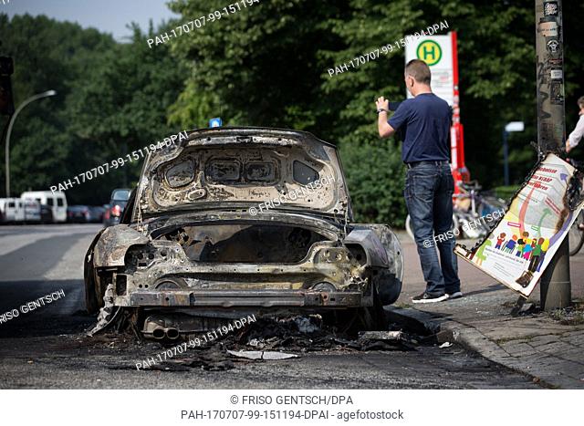A man takes a photograph of a car set alight during demonstrations against the G20 summit in Hamburg, Germany, 7 July 2017
