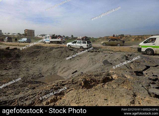 10 December 2023, Palestinian Territories, Khan Yunis: Palestinians drive their cars along a narrow stretch of Salah al-Din Road to avoid the crater left by...