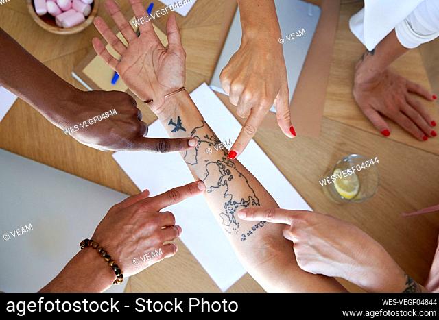 Business team pointing at map tattoo on colleague hand at office
