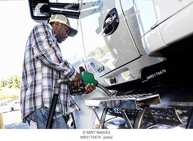 Black man truck driver putting diesel fuel in his truck at a truck stop