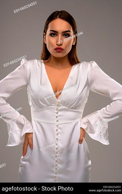 Confident female model wearing white shiny dress looking at camera studio portrait