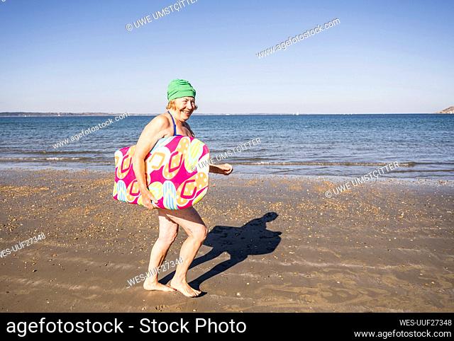 Happy senior woman running with surfboard at beach