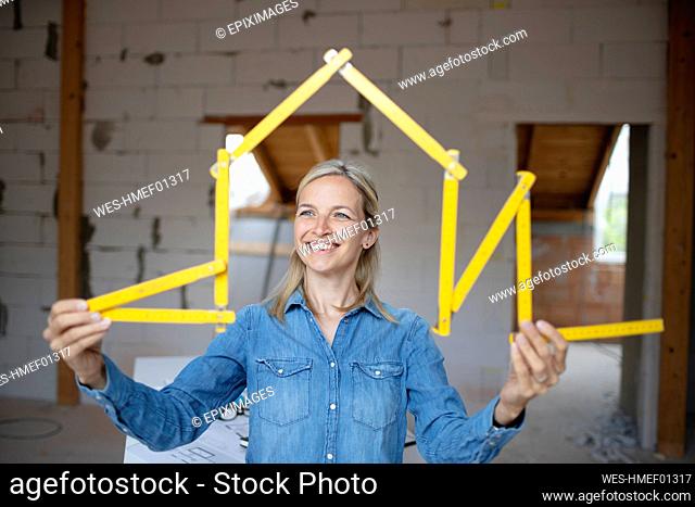 Happy female architect making house shape with folding ruler at site