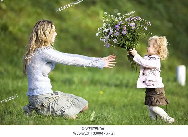 Daughter giving mother bunch of flowers, side view