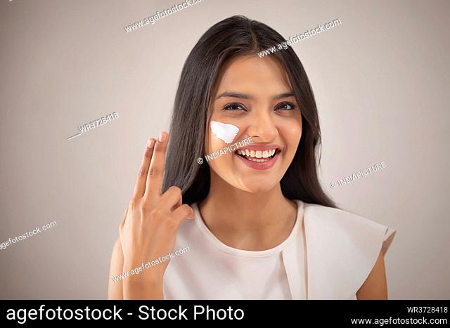 A CHEERFUL YOUNG WOMAN PUTTING CREAM ON FACE