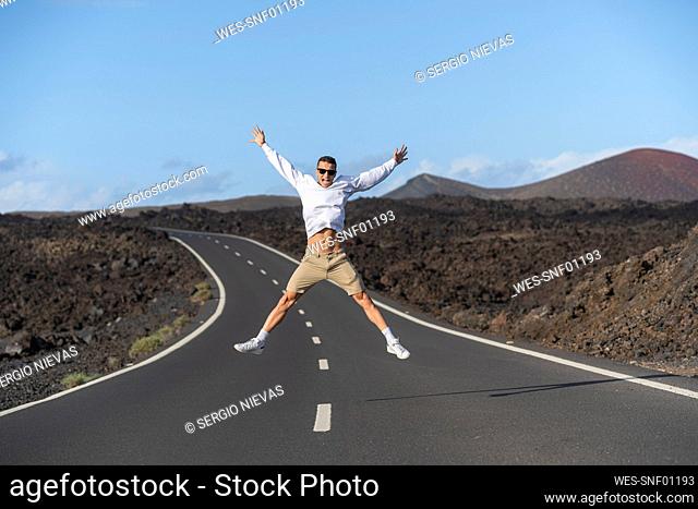 Cheerful male tourist with arms outstretched jumping over road