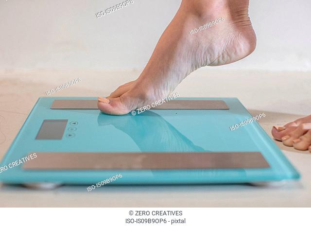 Young woman stepping onto weighing scales, close up of foot