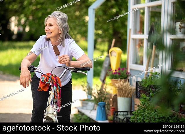 Happy woman. Cheerful woman on a bike eating ice-cream and looking happy