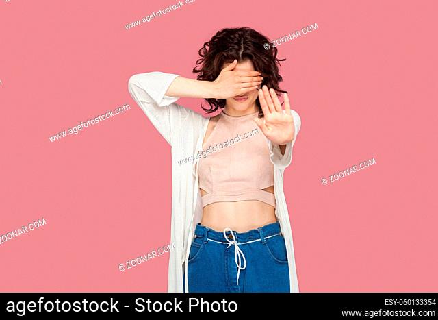 Stop, I don't want to see this. Portrait of brunette young woman with curly hairstyle in casual style standing, covering her eyes and showing stop hand