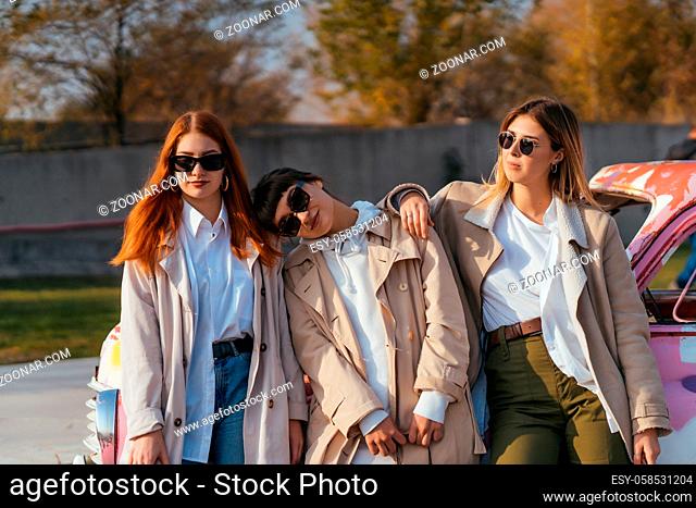 Young happy women with shopping bags posing near an old decorated car