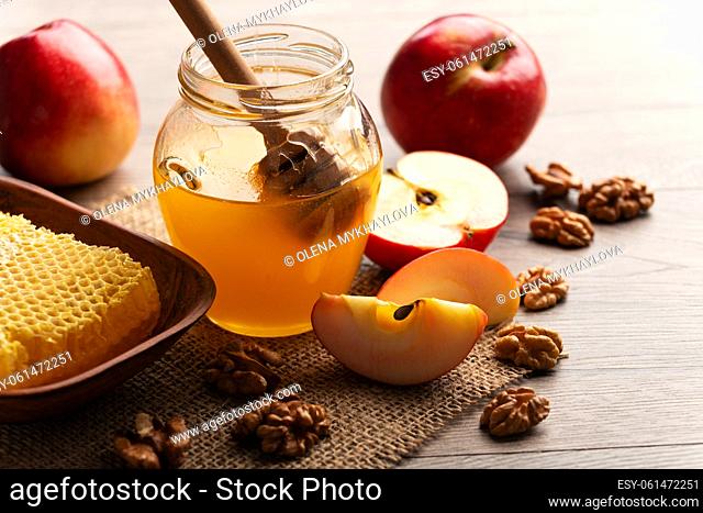 Mason jar with honey, honey dipper, honeycomb, red apples and walnuts on kitchen table
