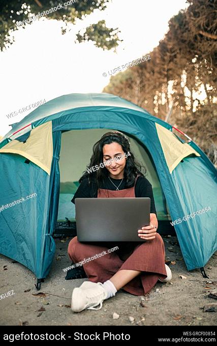 Young woman working on laptop in tent during weekend