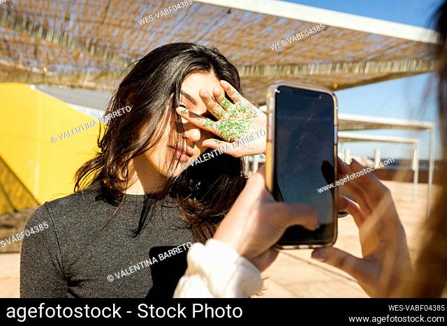Woman photographing female friend with glitter on palm during sunny day