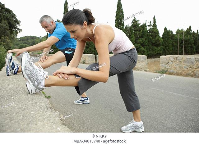 Pair, athletic, stretching exercise, sidewards, bent, wall, street,