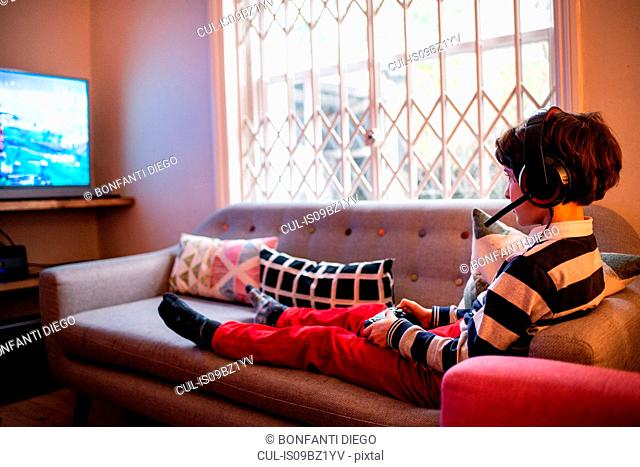 Boy sitting up on sofa playing video game using game controller