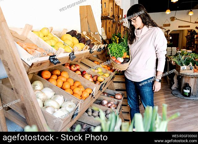 Female customer picking vegetables in basket from grocery store