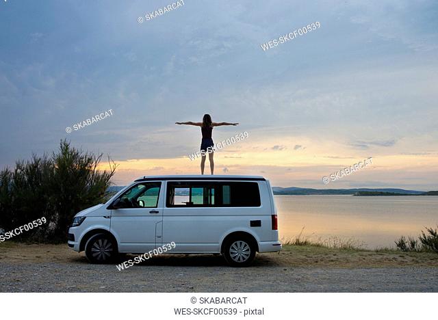 Woman standing on top of the van resting at sunset on the lake