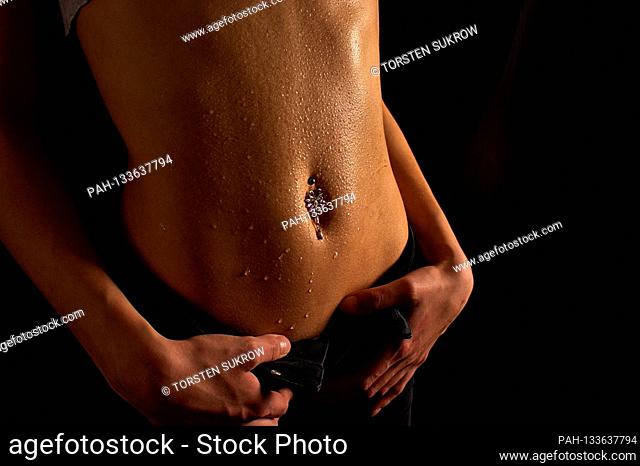 04/05/2016, detailed shot of a young woman with a free, flaughs and moist shiny belly and navel piercing sexy and lascivious with her hands on the waistband
