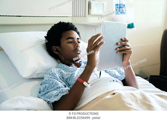 Black boy in hospital bed listening to digital tablet