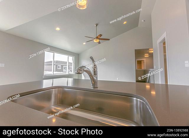 Stainless steel sink and faucet inside the kitchen of a new house. The room is well lit by the bright sunlight and warm ceiling lights