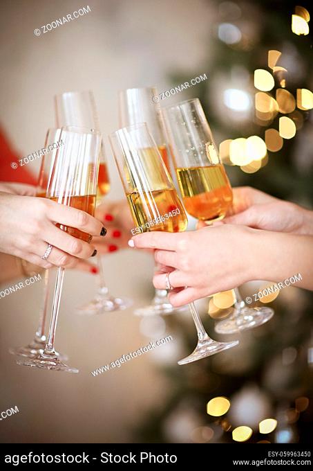 Unrecognizable female friends clinking glasses of champagne and proposing toast during Christmas celebration