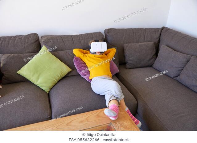 six years old child lying comfortably on a brown sofa with virtual reality headset glasses