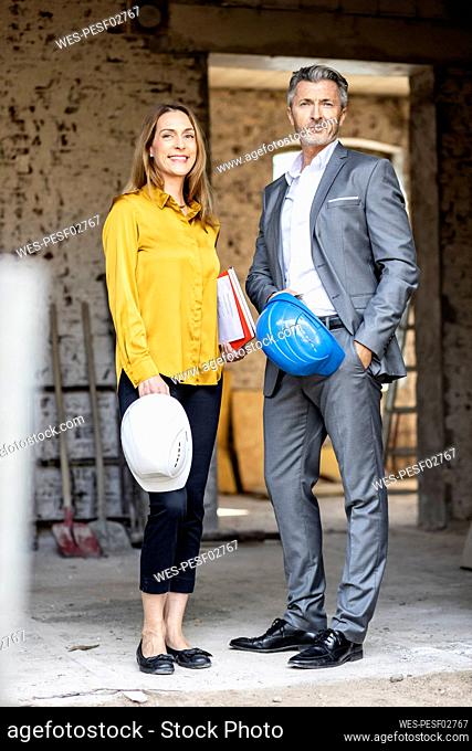 Smiling female architect with hardhat standing with male client at construction site