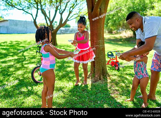 Father and daughters playing with water squirt gun in summer backyard