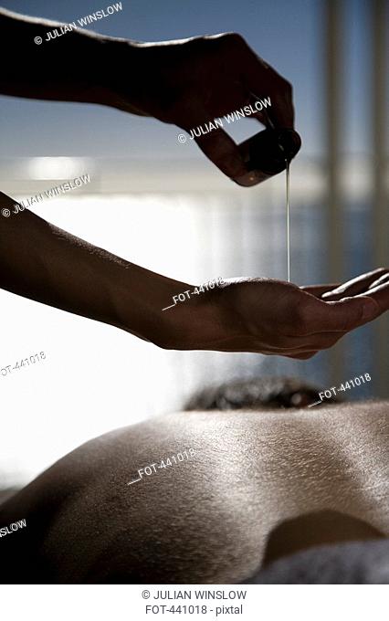 Close-up of a woman pouring oil onto her hands before massaging a man's back