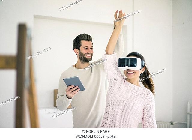 Man lifting woman's arm wearing VR glasses in new home