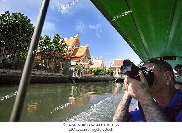 A tourist photographs temples from a longboat on one of Bangkoks many canals, Thailand