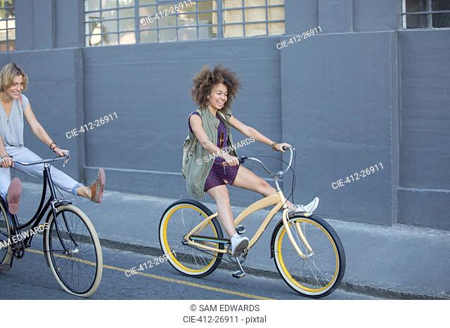 Playful women coasting on bicycles down urban street