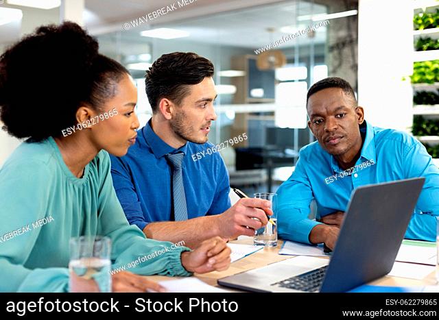 Diverse business people using laptop and discussing in modern office