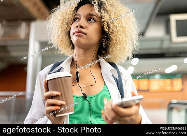 Thoughtful woman holding disposable cup and smart phone