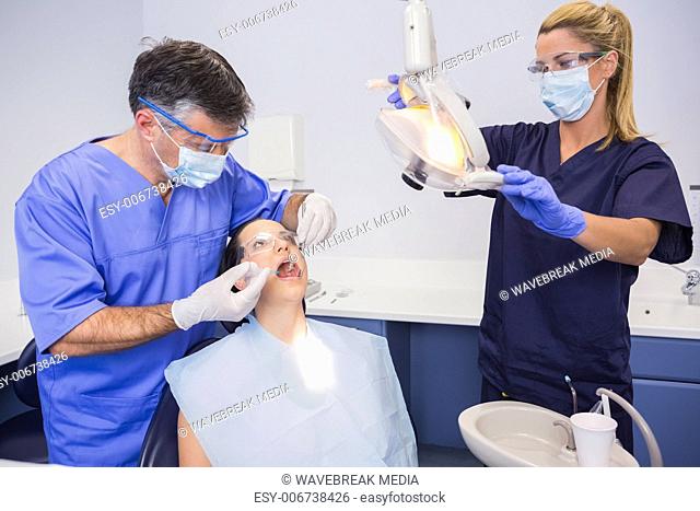 Dentist doing injection to his patient and nurse adjusting the light