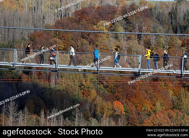 22 October 2022, Saxony-Anhalt, Hasselfelde: Visitors walk over the suspension bridge at the Rappbode Dam and enjoy the autumnal colorful forest