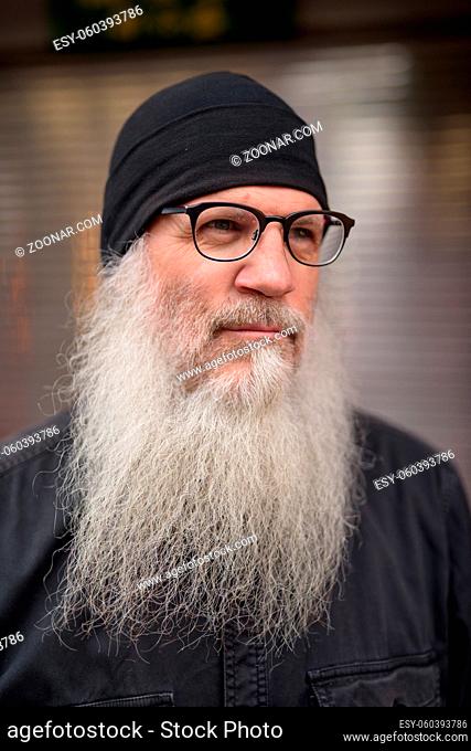 Portrait of mature handsome hipster man with long beard wearing eyeglasses and hat in the streets outdoors