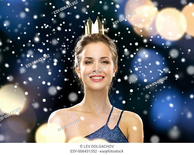 people, holidays, royalty and glamour concept - smiling woman in evening dress wearing golden crown over night lights and snow background