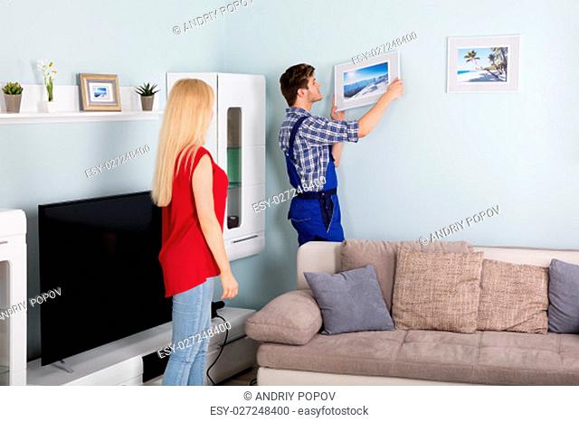 Young Woman Showing Male Carpenter For Hanging Picture Frame On Wall At Home