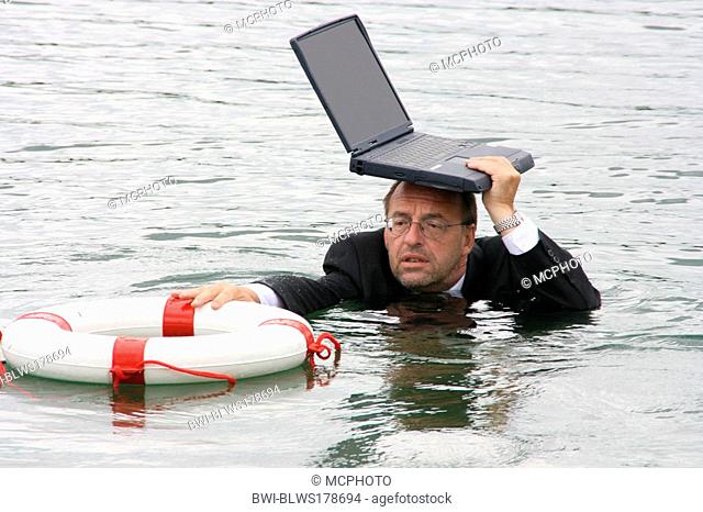 businessman in deep water holdig laptop over his head and grabbing to life belt