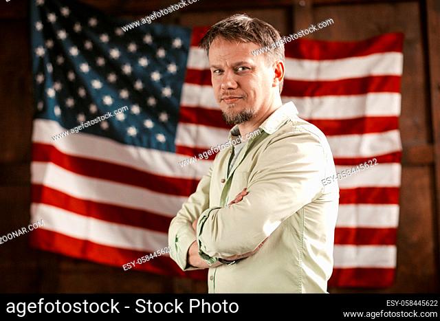 Charming American Boss Is Confidently Looking Forward With His Hands Folded On His Chest Against The Backdrop Of A Wooden Wall With An American Flag