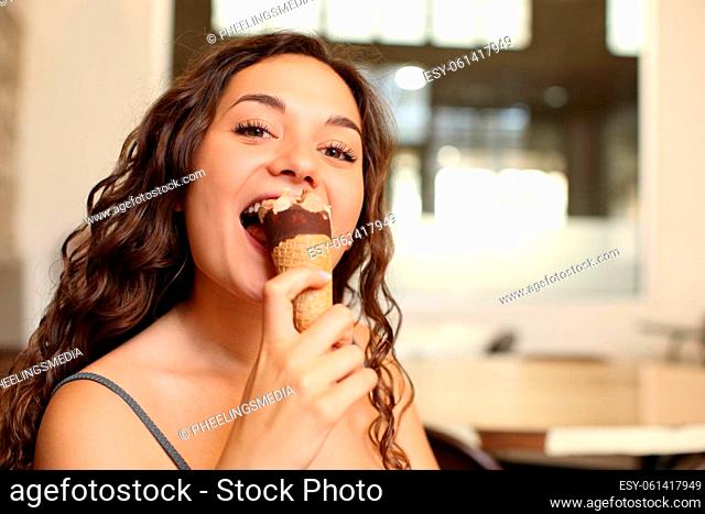 Happy woman eating ice cream looking at you in a bar