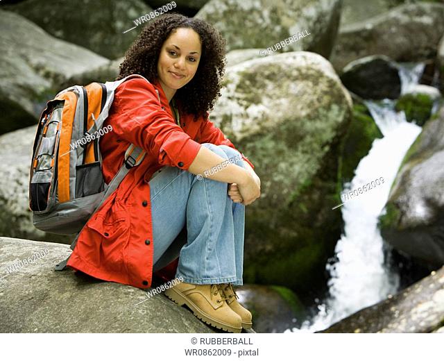 Portrait of a young woman sitting on a rock and smiling