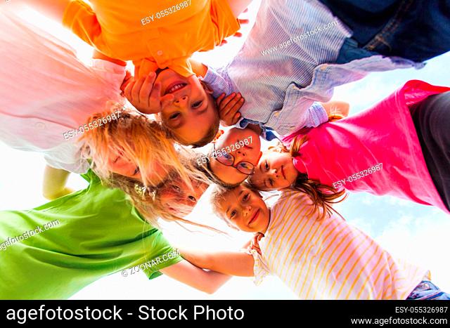 A huddle of school kids in colorful t-shirt standing shoulder to shoulder looking down at camera, close up view. Teamwork concept