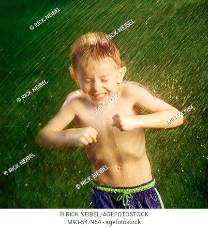 Young boy reacting to being sparyed with water hose