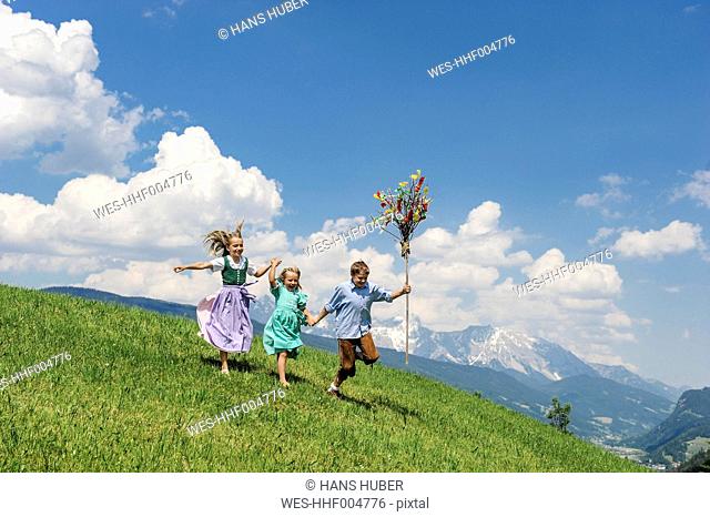Austria, Salzburg State, Altenmarkt-Zauchensee, three children with Palmbusch running on alpine meadow