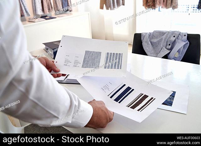 Mature male owner examining fabric swatches on table in clothing design studio